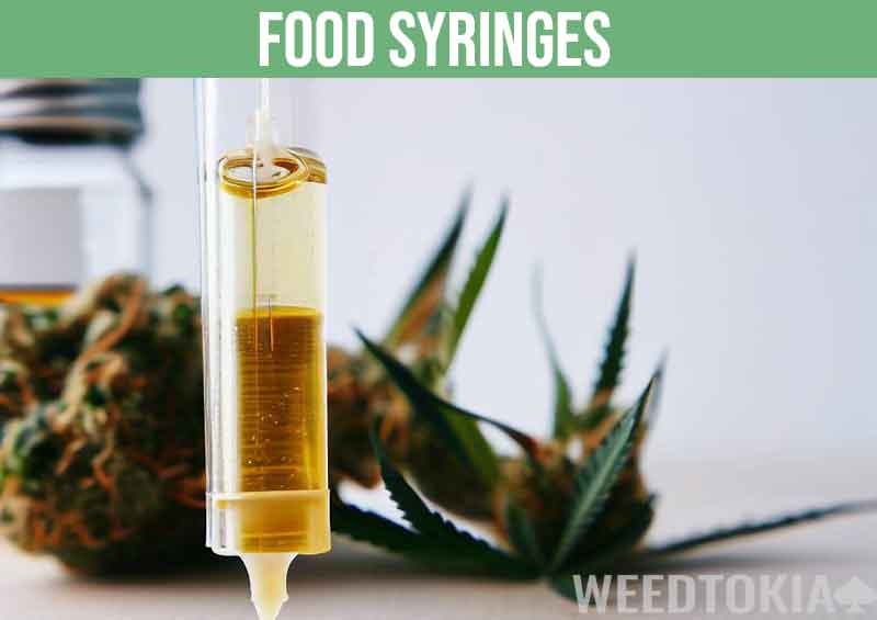 Food syringe filled with cannabis oil next to weed